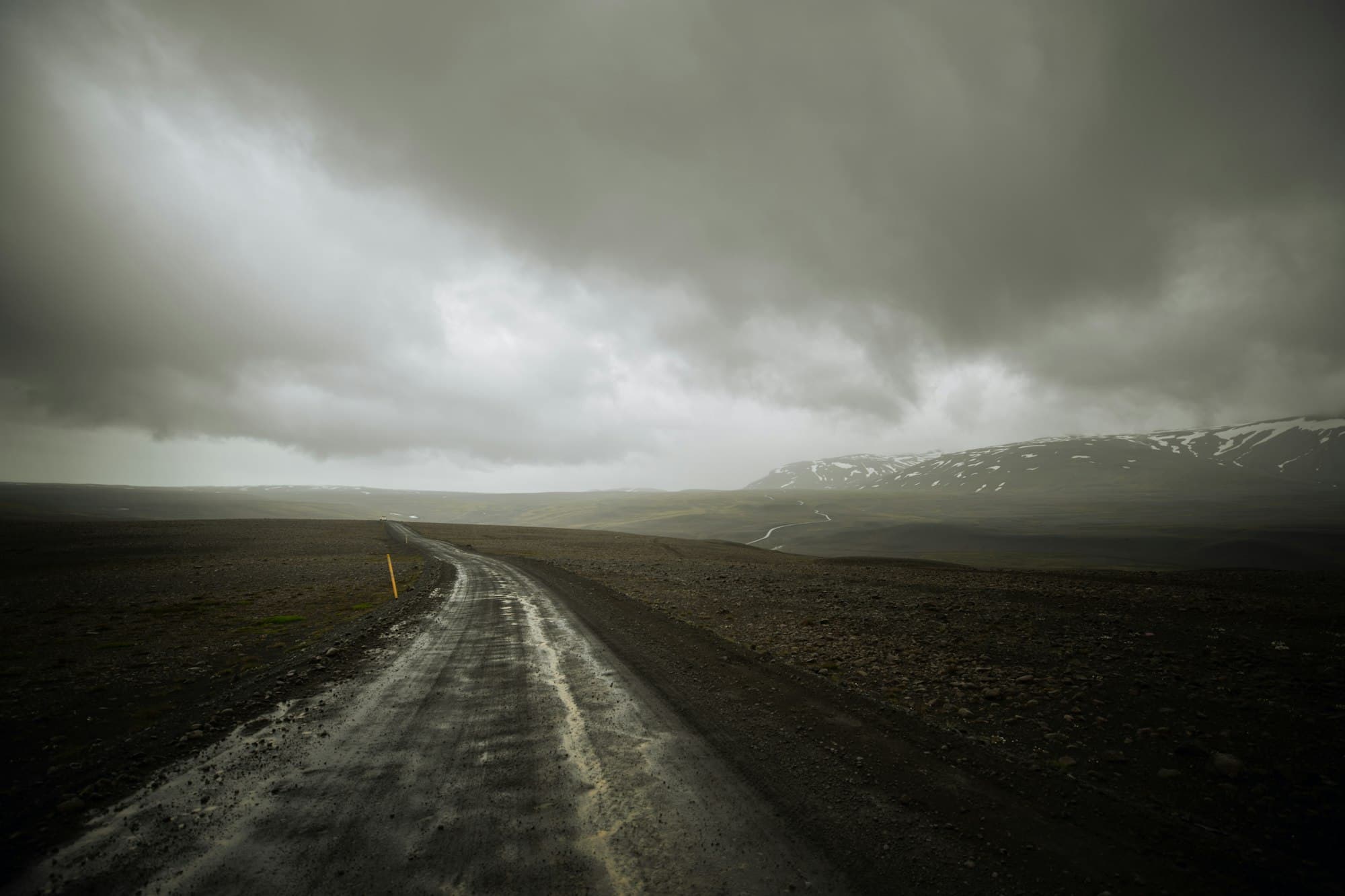 Empty road cutting through Iceland's green highland landscape under a dramatic grey sky